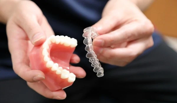 손에 들고 있는 인비절라인 투명 교정 장치와 치아 모형 / Person holding Invisalign clear aligner and dental mold for orthodontic care